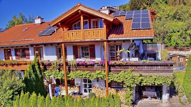 A two-story chalet with a sloped roof, wooden balconies, and solar panels.