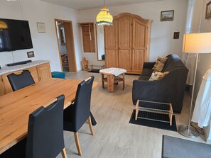 A dining area with a wooden table and chairs, a sofa, a TV, and a cabinet.