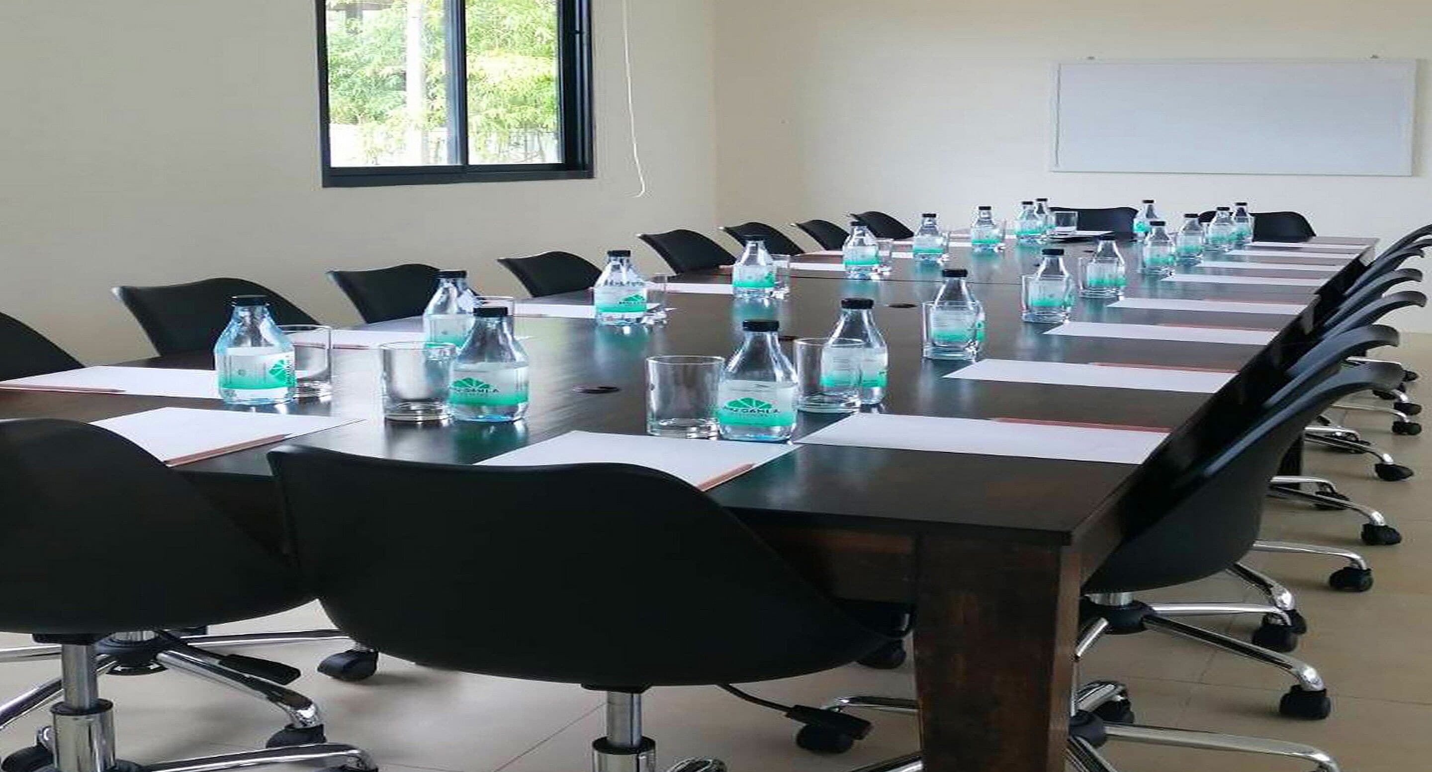 A conference room with a long table, black chairs, and water bottles on the table.