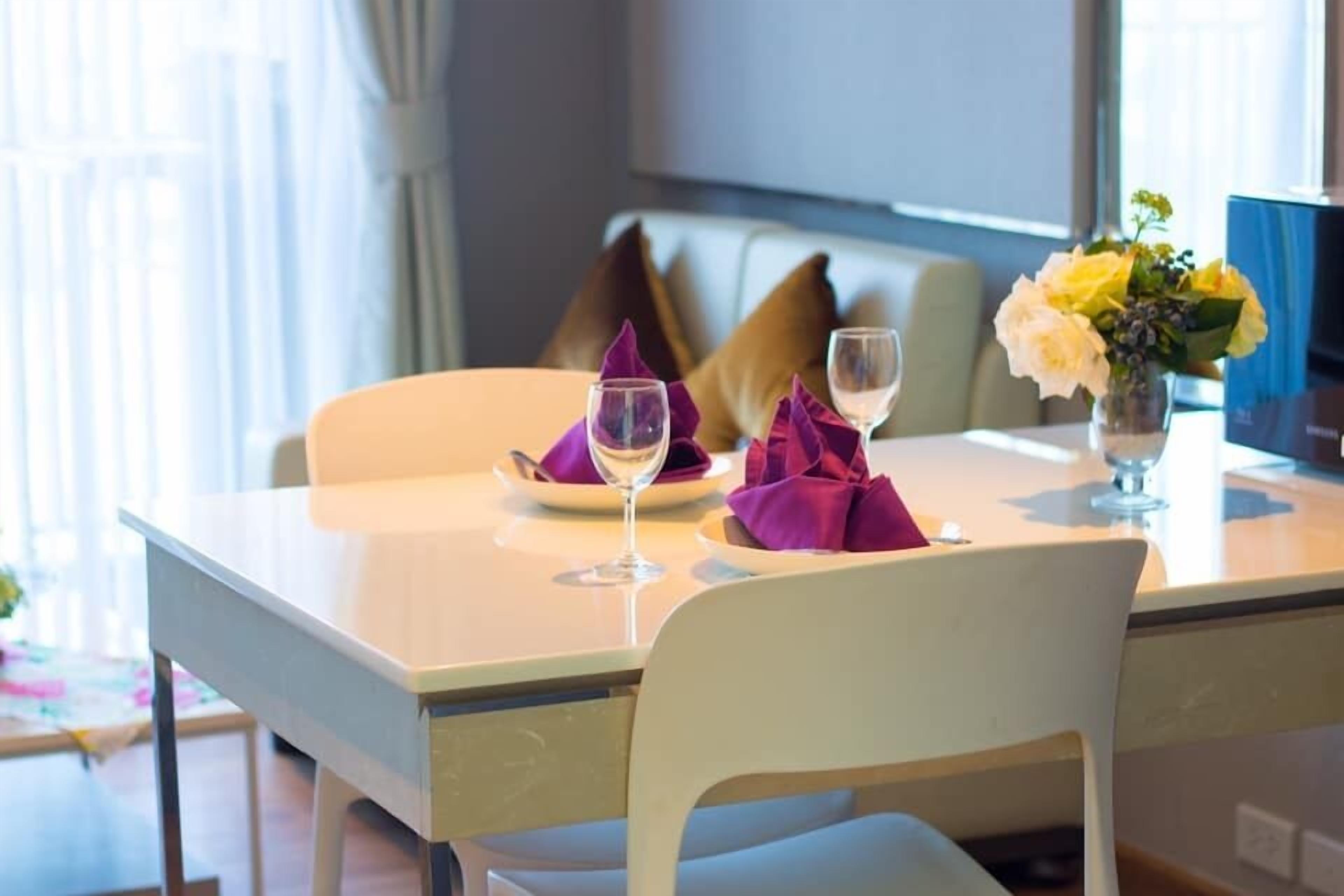 Ein Esstisch, gedeckt mit einer weißen Tischdecke, violetten Servietten und einer Vase mit gelben Blumen.
