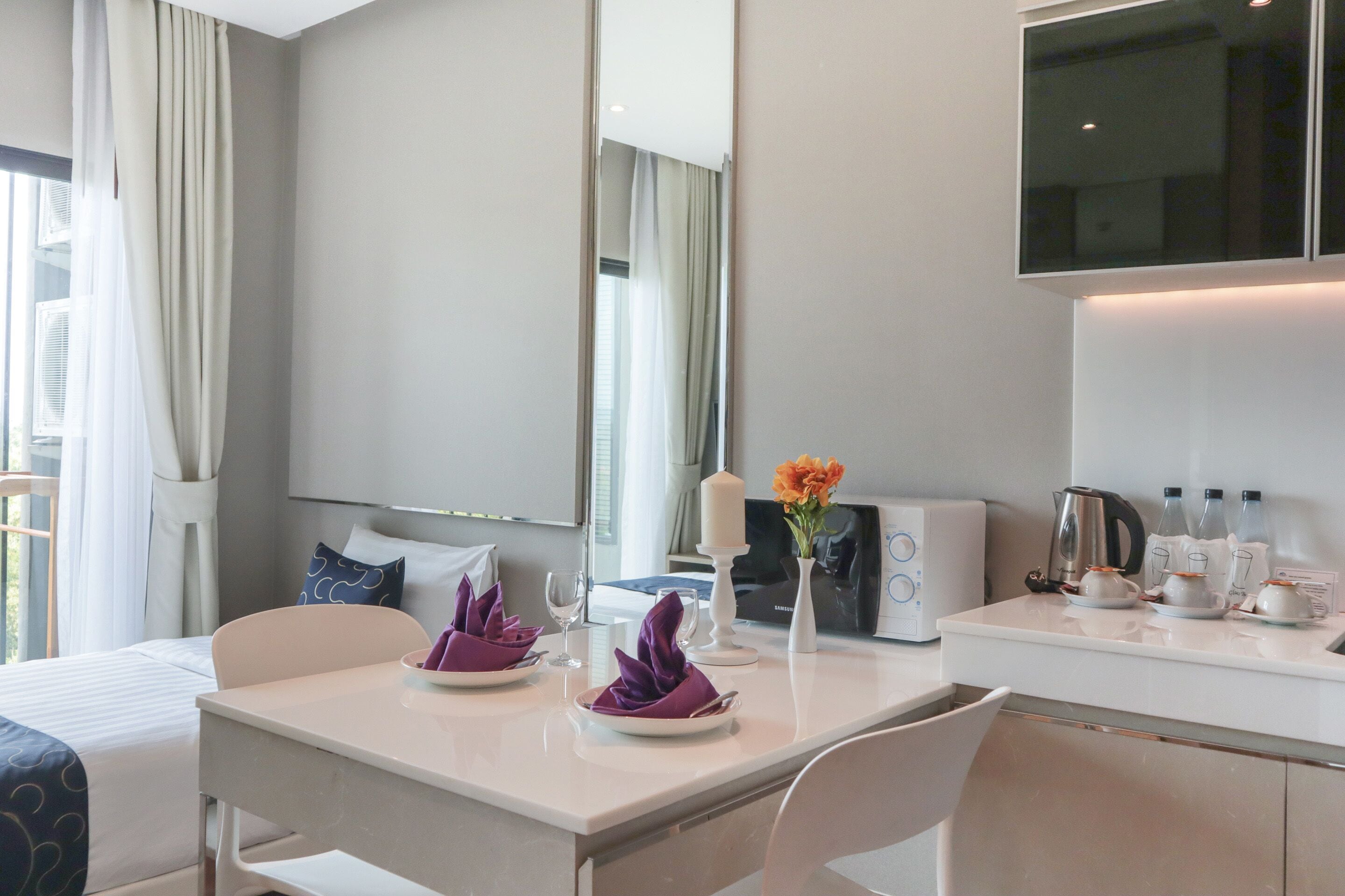 A modern hotel room with a dining area, a bed, a TV, and a kitchenette.
