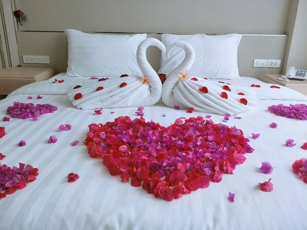 Un lit avec du linge de maison blanc, une composition en forme de cœur faite de pétales de roses et deux serviettes en forme de cygne.