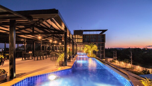 Una piscina con una zona de estar techada y un edificio moderno al fondo.