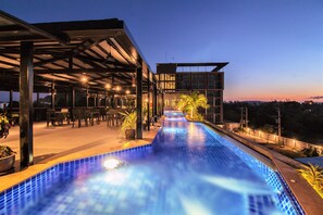 Une piscine dotée d’un espace de repos couvert, avec un bâtiment moderne en arrière-plan.