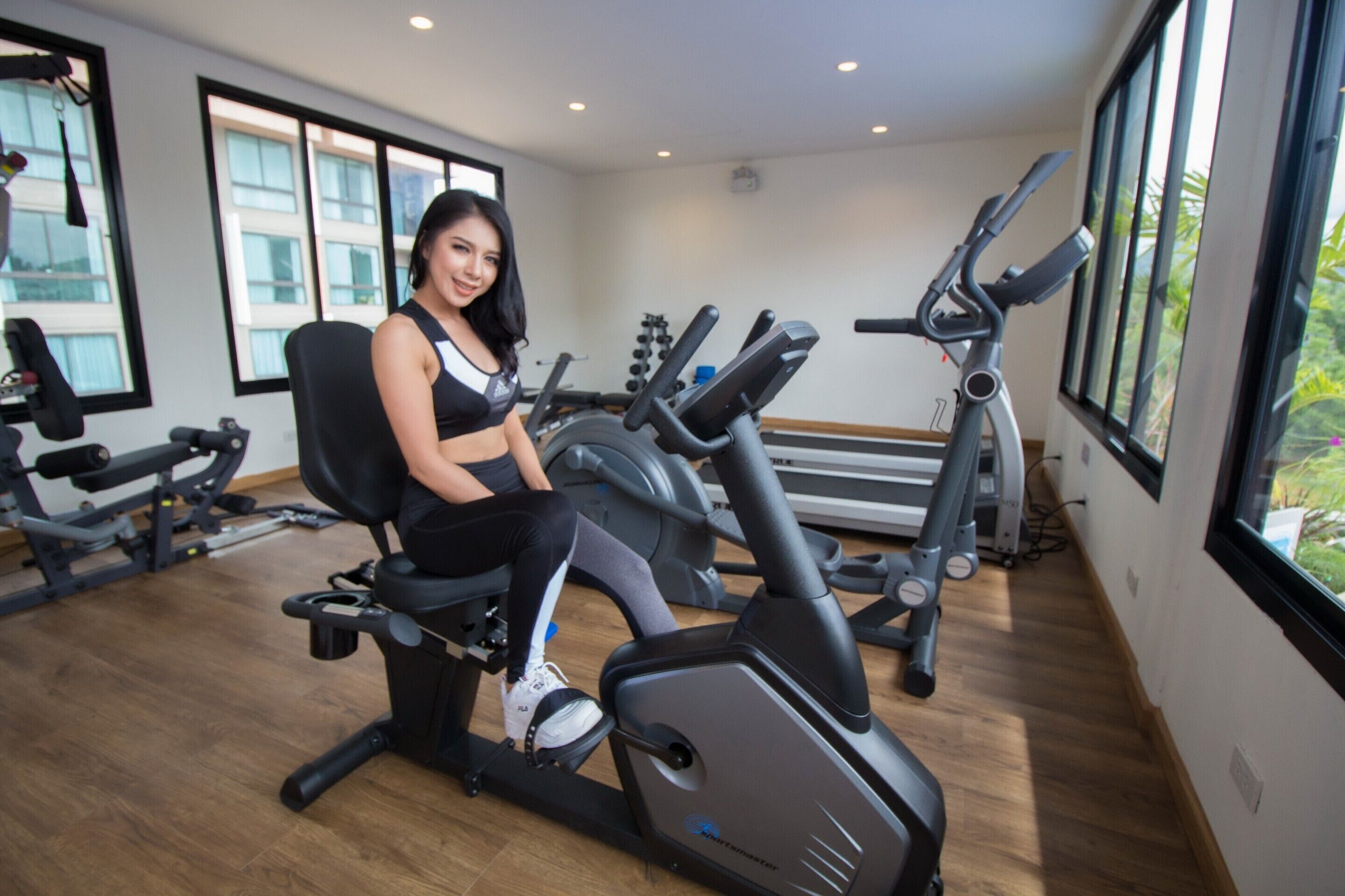 Un gimnasio con equipo de ejercicio, ventanas amplias y piso de madera.