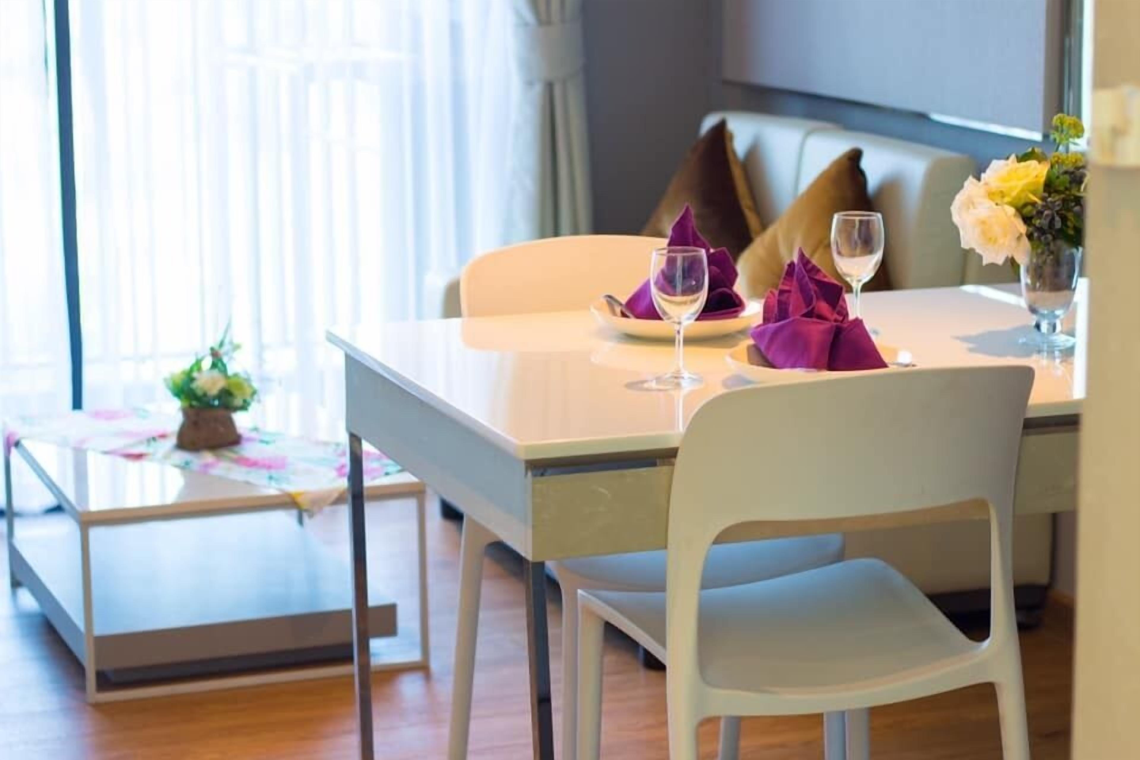 A dining area with a table set for two, a vase with flowers, and a window with curtains.
