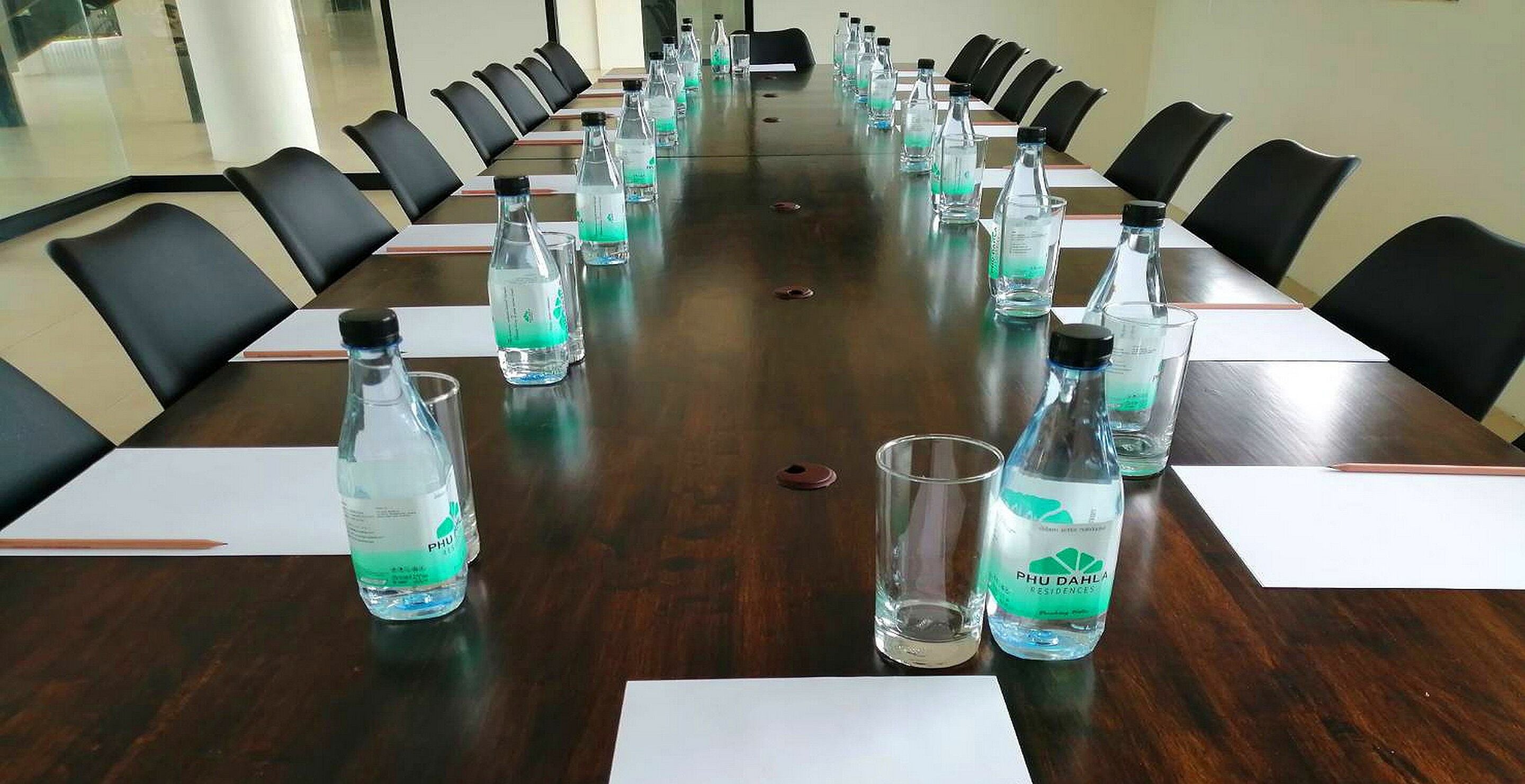 A conference room with a long table, black chairs, and water bottles labeled "PHU DAHL RESIDENCES".