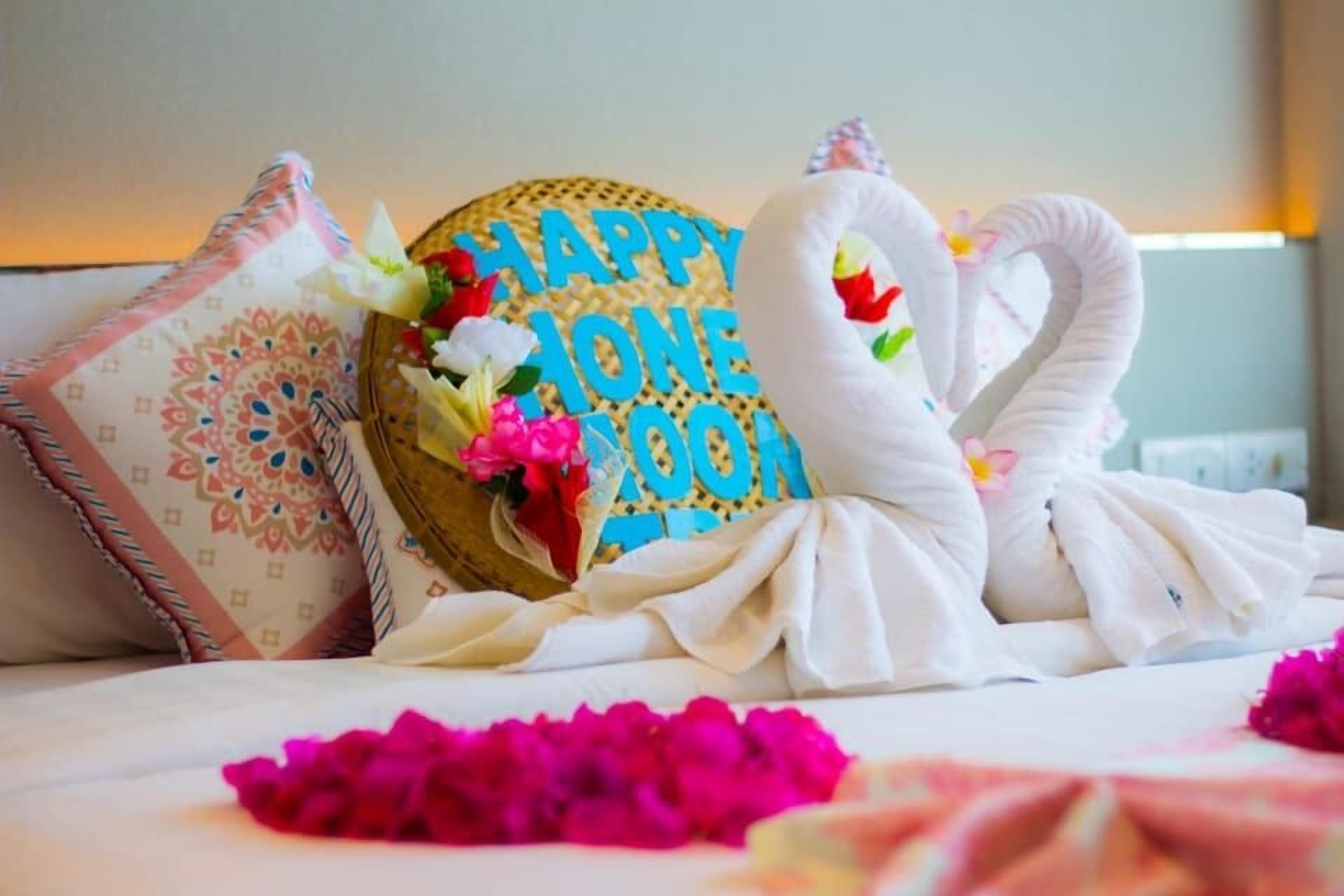 Una cama con un cojín decorativo con forma de cisne, un letrero que dice 'Feliz Luna de Miel' y un arreglo floral.