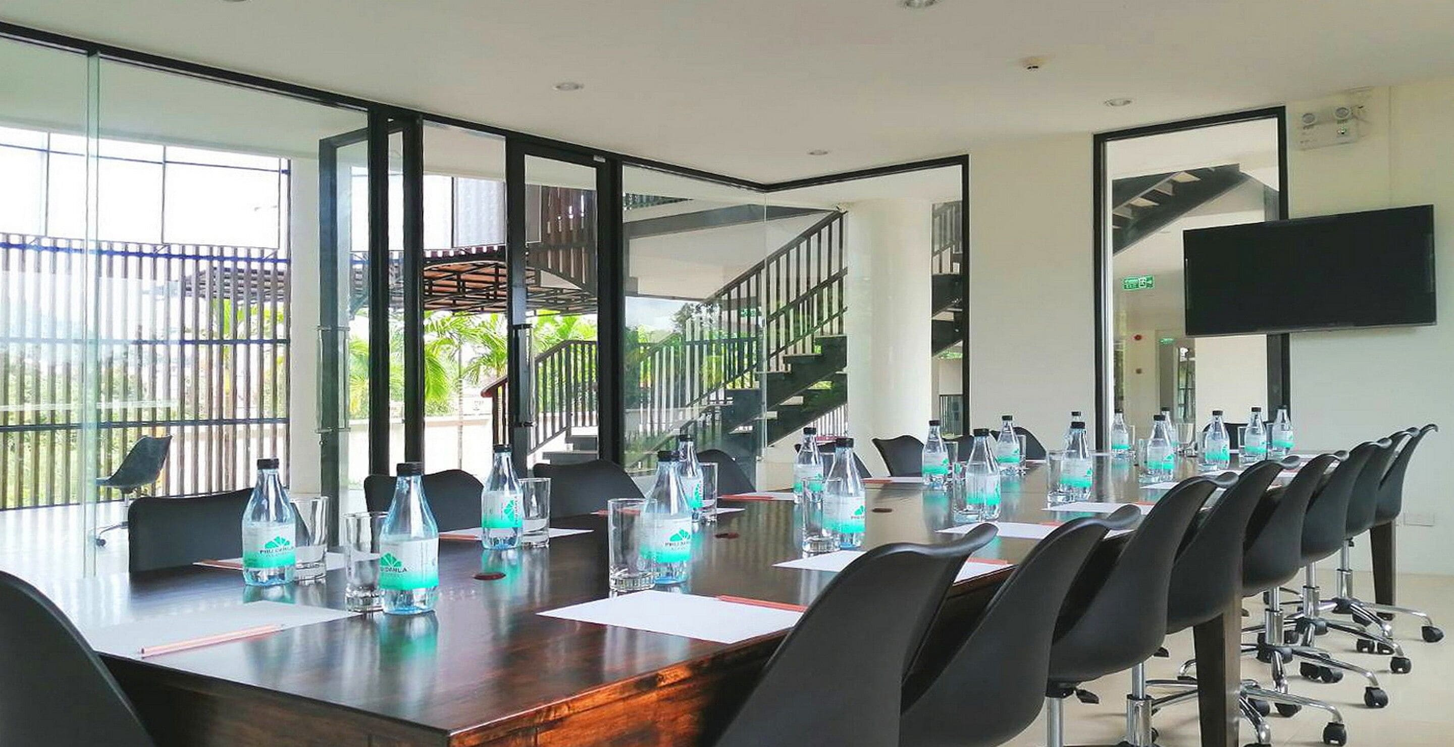 Une salle de conférence avec une longue table, des chaises et des bouteilles d’eau.