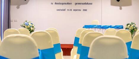 A room with rows of chairs, a stage with a banner, and two wall-mounted speakers.