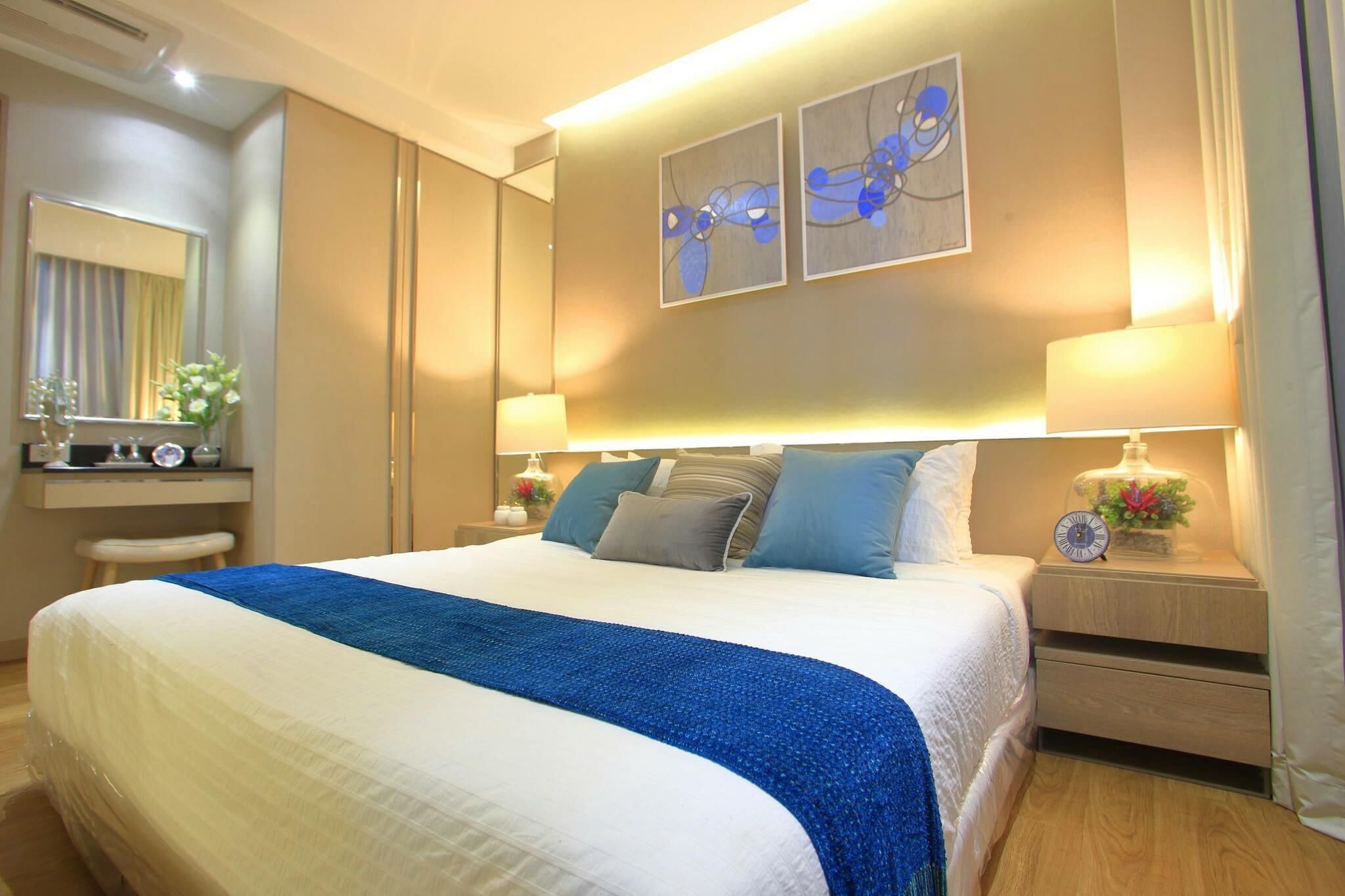A hotel room with a large bed, bedside tables, a mirror, and artwork on the wall.