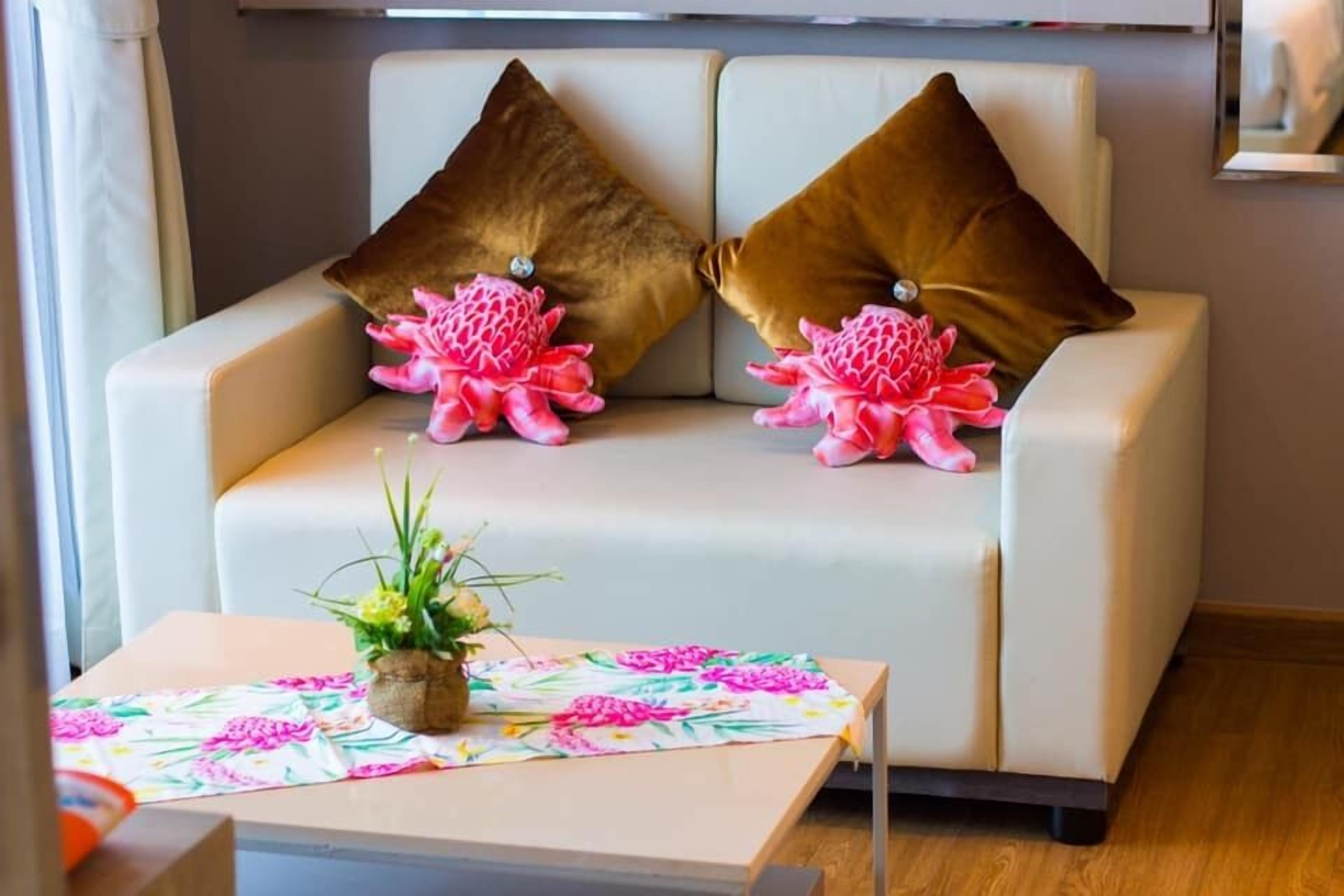 A modern living room with a beige sofa, two brown pillows, and a floral table runner.