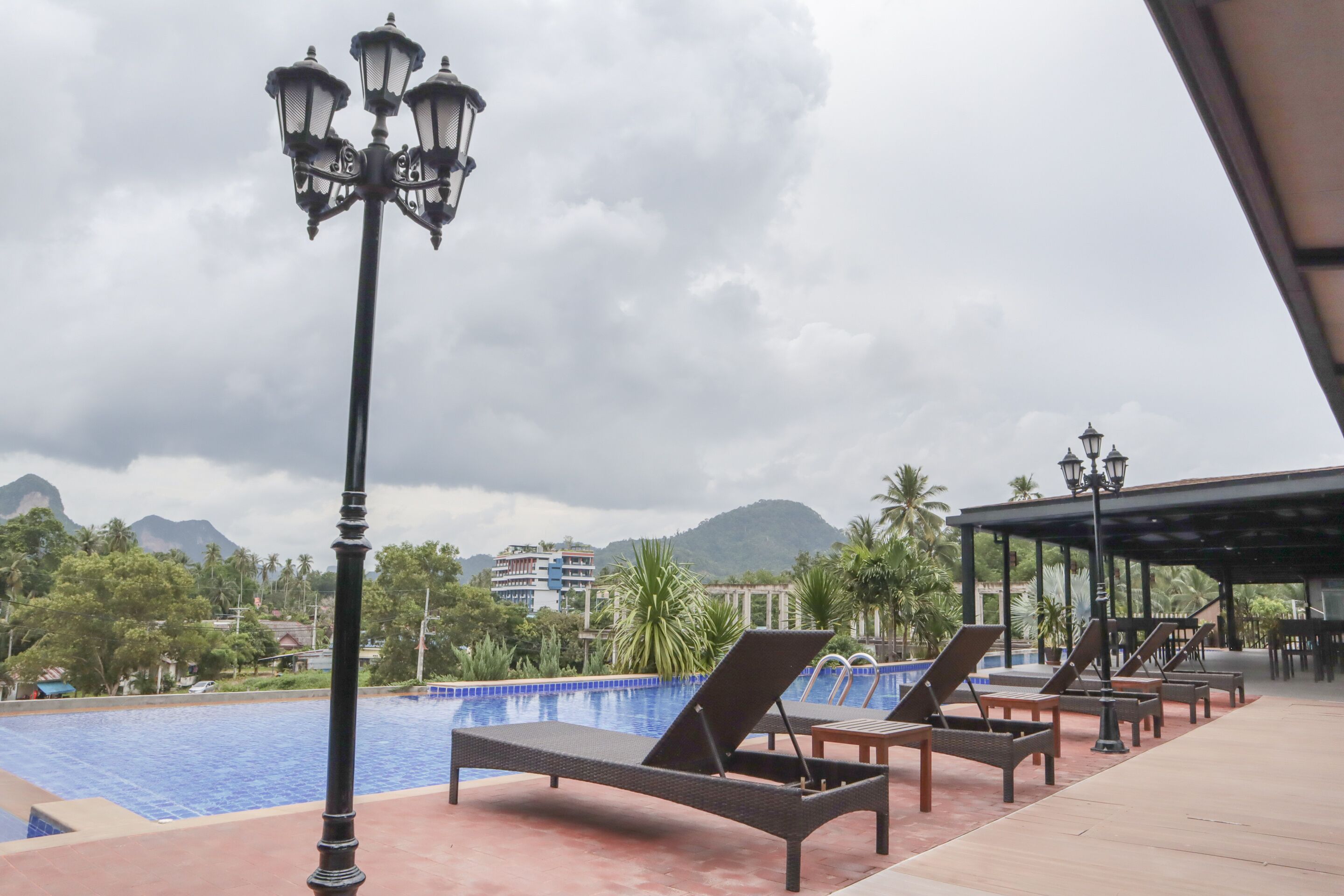A poolside area with lounge chairs and a lamp post, overlooking a swimming pool with a mountain backdrop.
