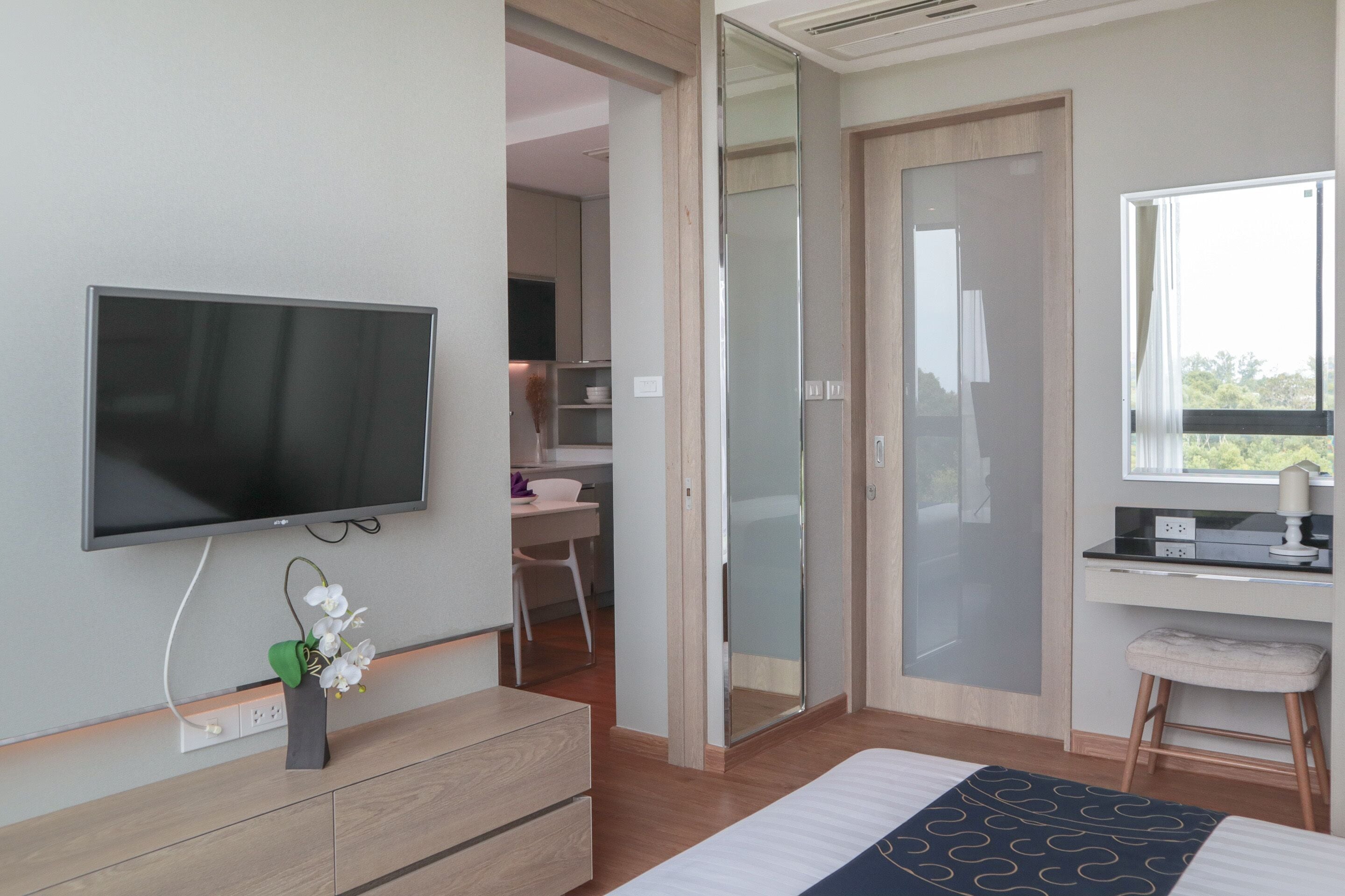 A modern bedroom with a TV, a desk, and a chair, a sliding door, and a window with a view.