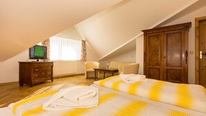 A bedroom with two beds, a wooden dresser, a television, and a window with curtains.