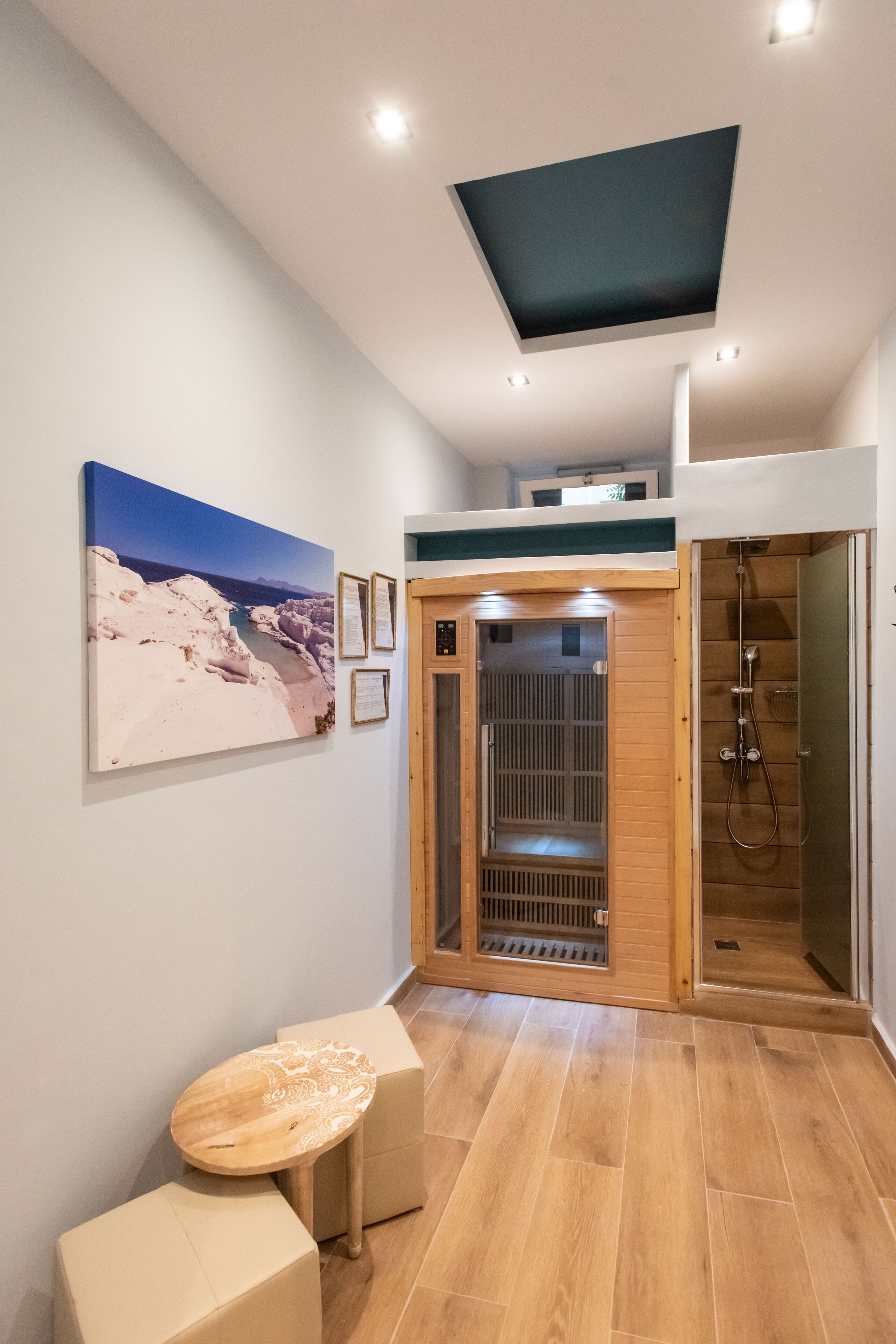 Une salle de bain moderne avec une cabine de douche en bois, une petite table en bois et un tableau représentant un paysage, encadré, accroché au mur.