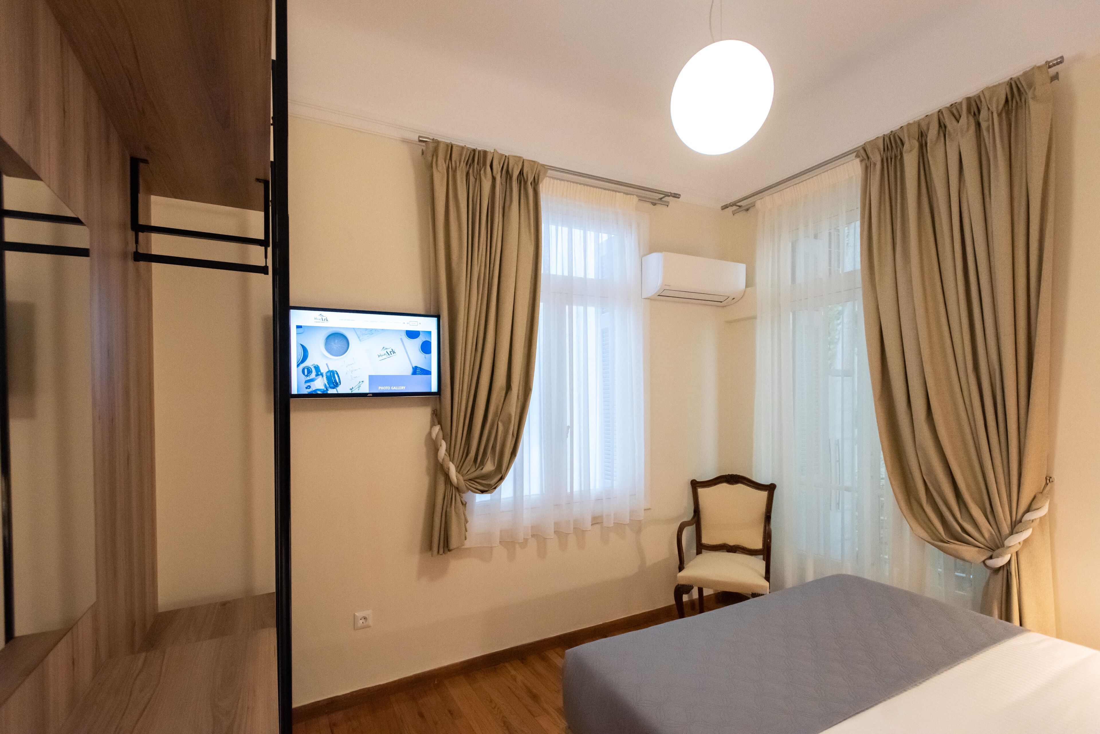 A hotel room with a bed, a chair, a TV on the wall, and curtains.
