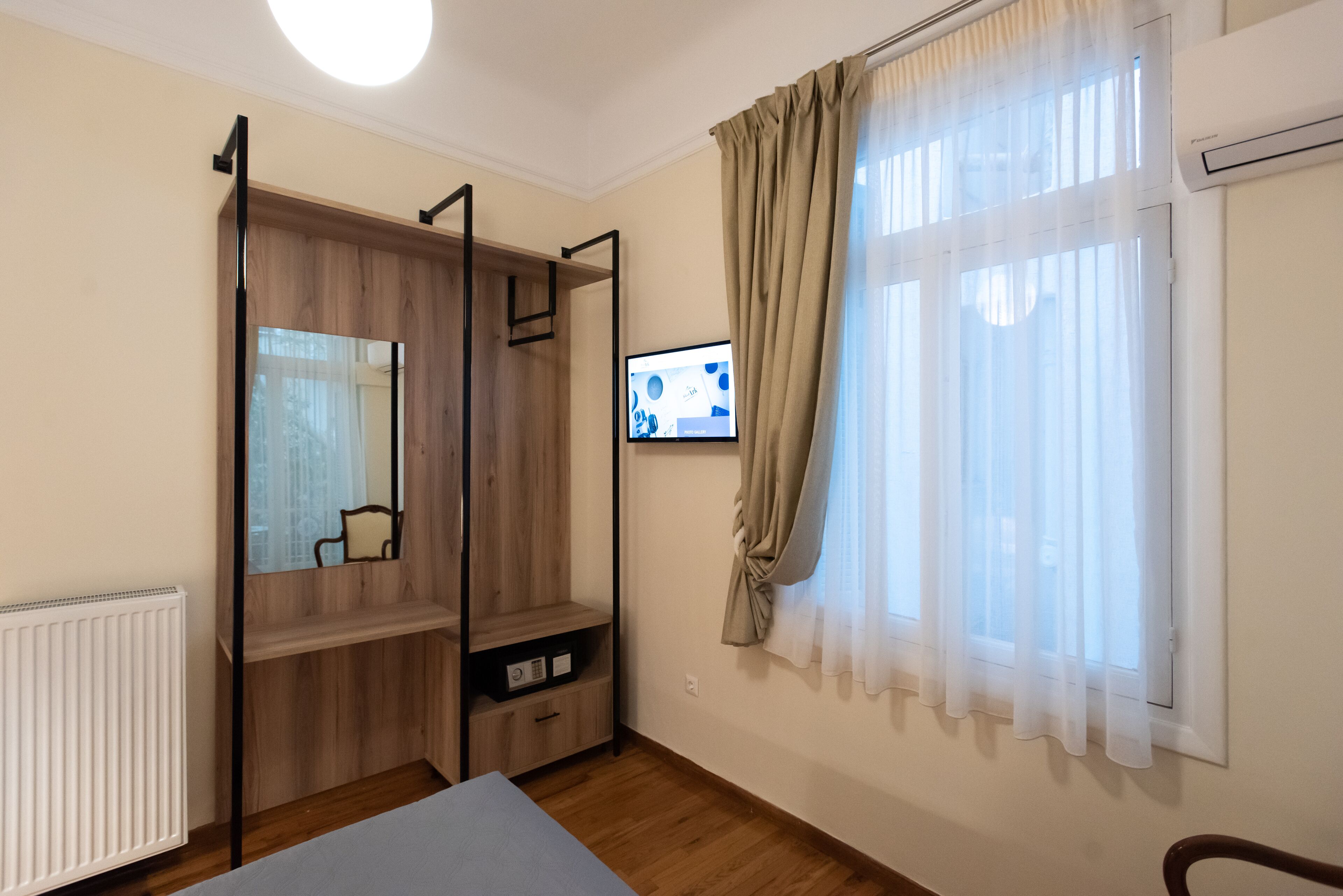A bedroom with a wooden wardrobe, a bed, a TV, and a window with curtains.