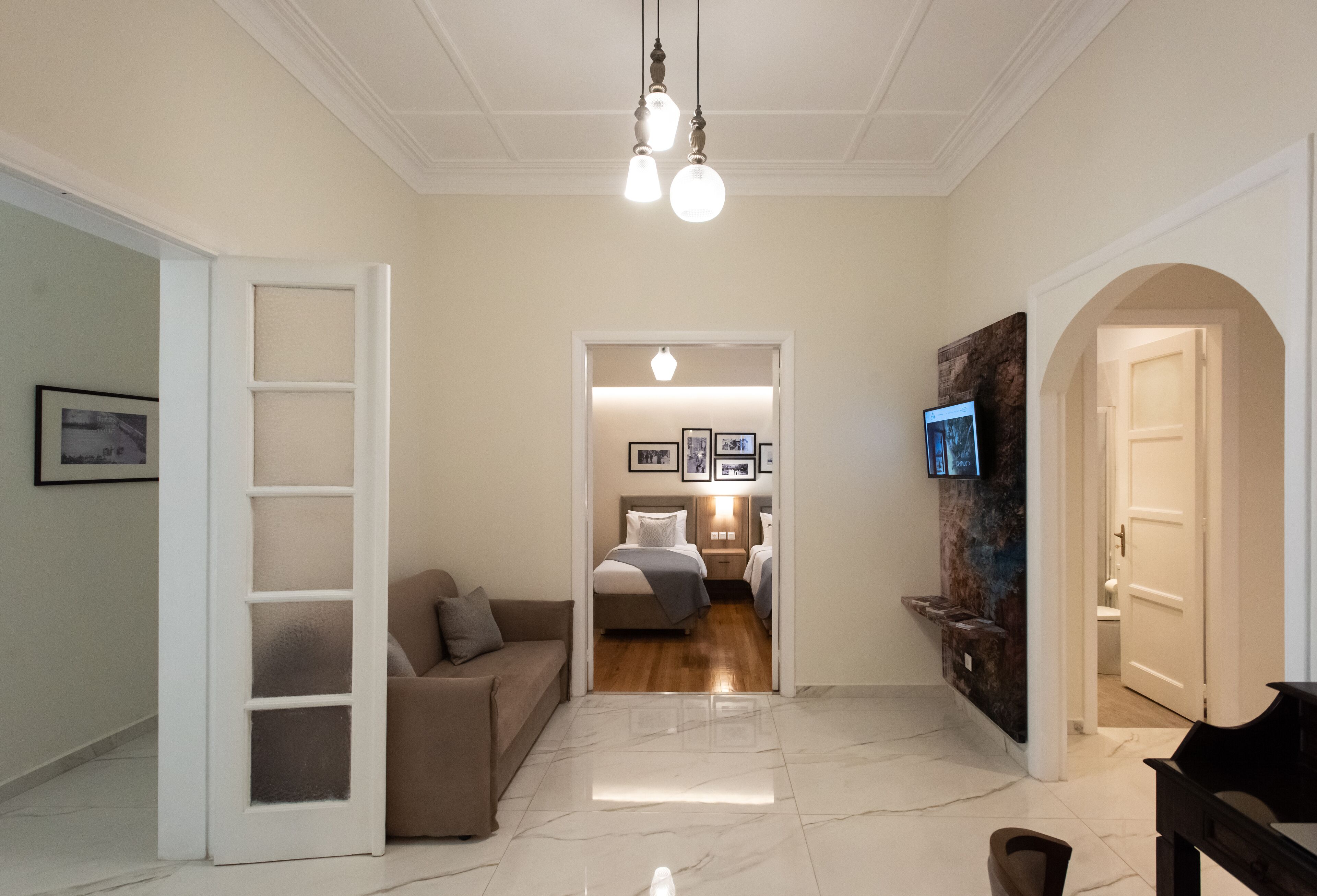 A spacious living area with a sofa, a piano, and a hallway leading to a bedroom with a bed and a TV.