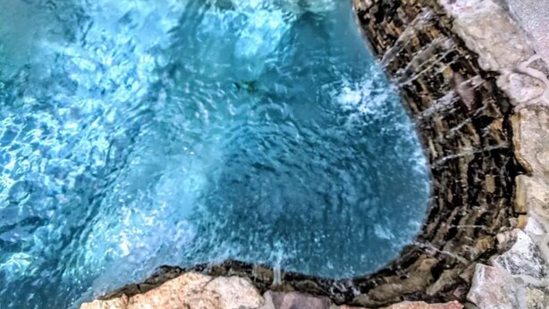 Une piscine à l’eau claire, entourée de murs de pierre et bordée de rochers.
