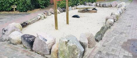 Zona de juegos arenosa con rocas grandes y un conjunto de columpios de madera.