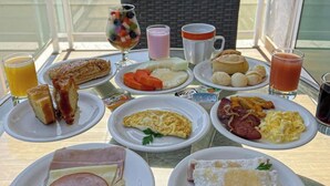 Ein Frühstücksbuffet mit verschiedenen Speisen und Getränken auf einem Glastisch im Freien.