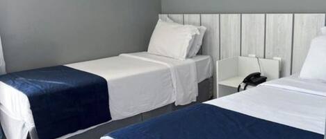 A hotel room with two beds, a bedside table with a phone, an air conditioning unit, and a framed picture on the wall.