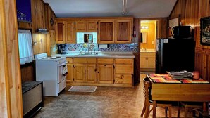 A compact kitchen with wooden cabinets, a stove, a refrigerator, and a tiled backsplash. - Cozy studio cabin close to Lake Michigan. (Frankfort)