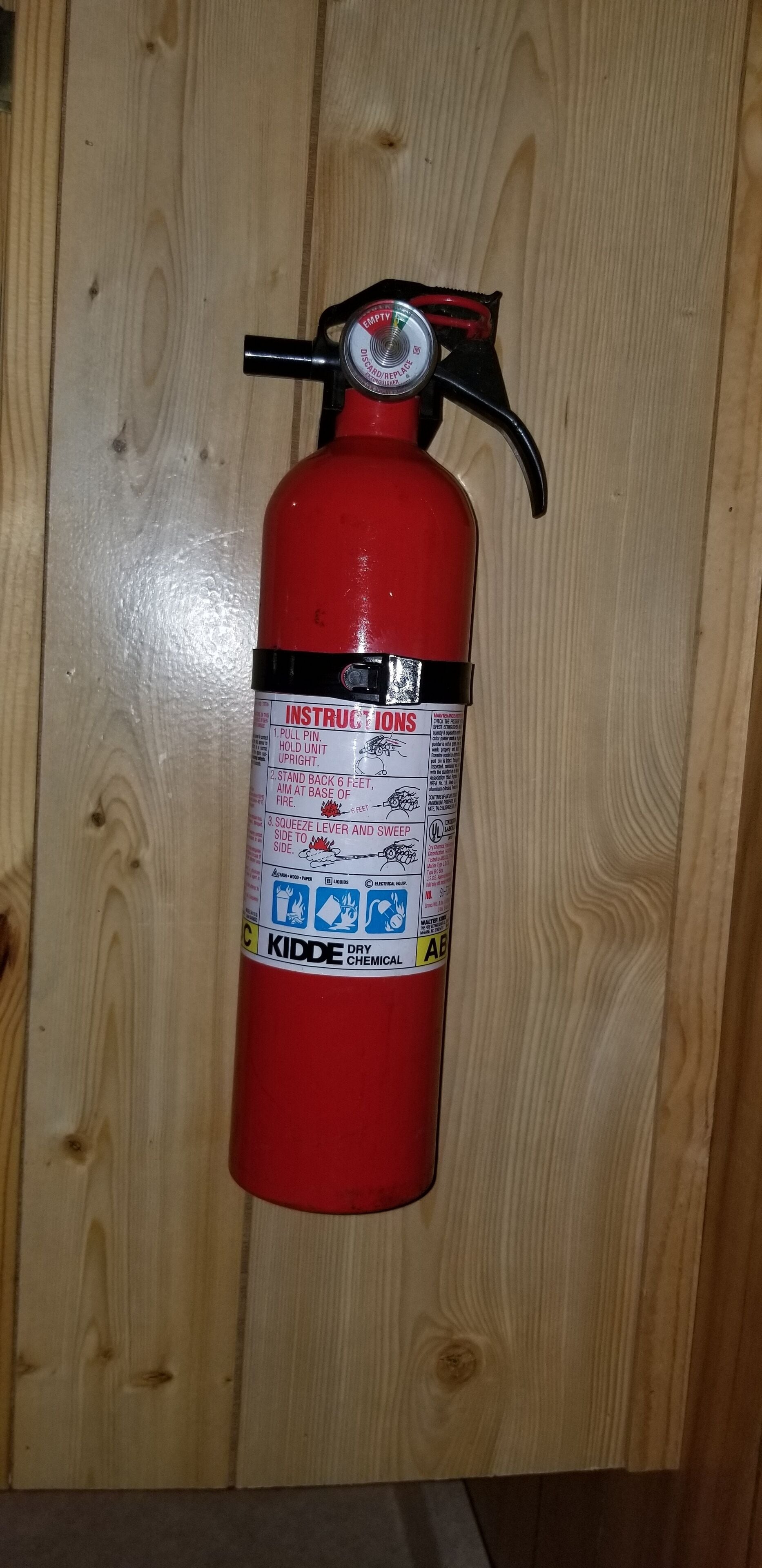 Ein roter Feuerlöscher an einer Holzwand befestigt.
