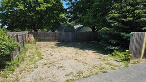A backyard with a gravel area, a wooden fence, and a green shed. - Cozy studio cabin close to Lake Michigan. (Frankfort)
