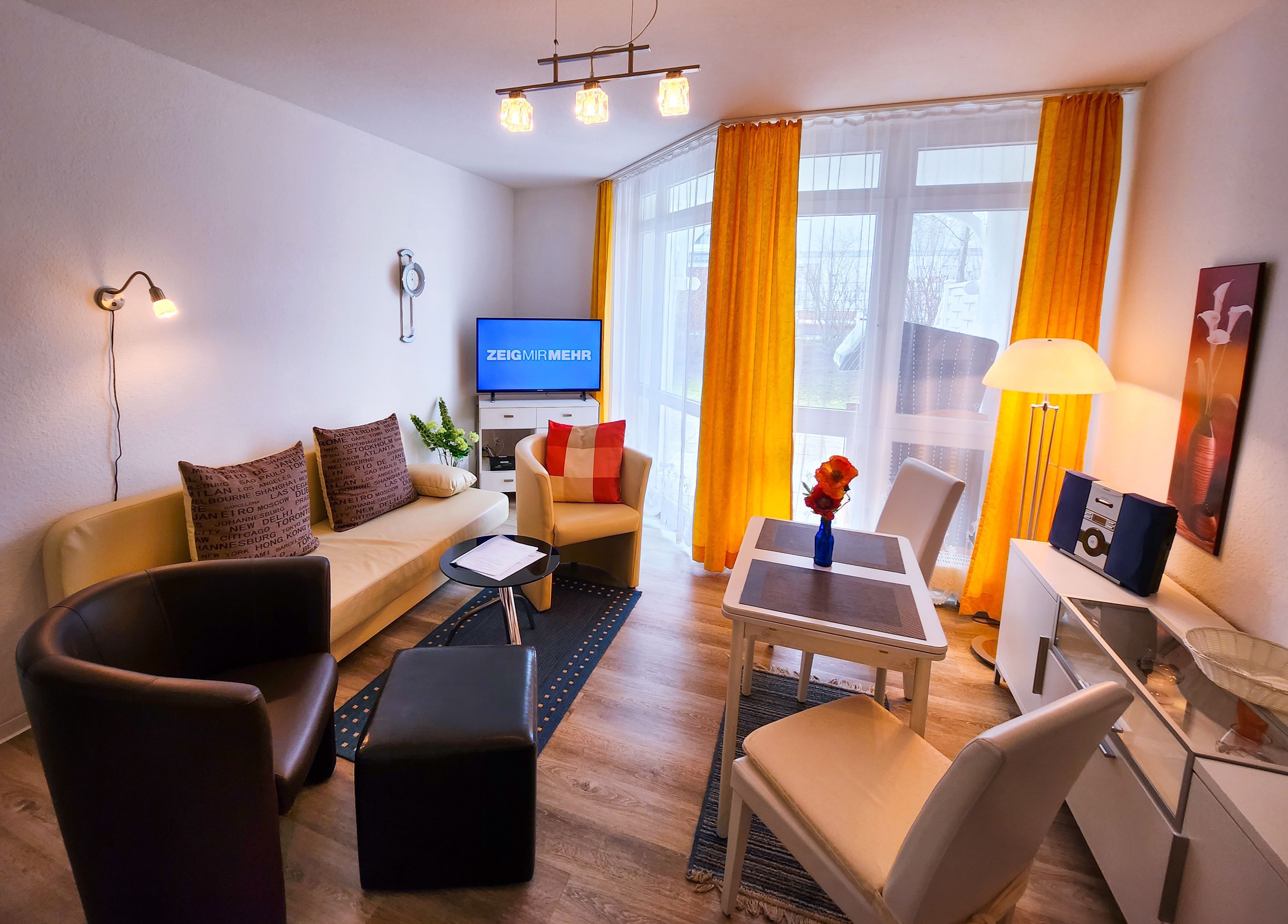 Ein modernes Wohnzimmer mit einer Couch, Sesseln, einem Couchtisch, einem Fernseher und einer Lampe.
