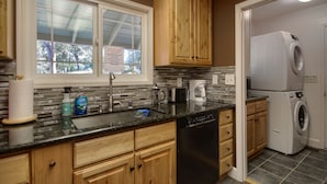 A kitchen with wooden cabinets, a dishwasher, a washing machine, and a window with a view of trees. - The Retreat@Lakeside Hot Tub/Views/Fast WiFi Near Yosemite! (Mariposa)