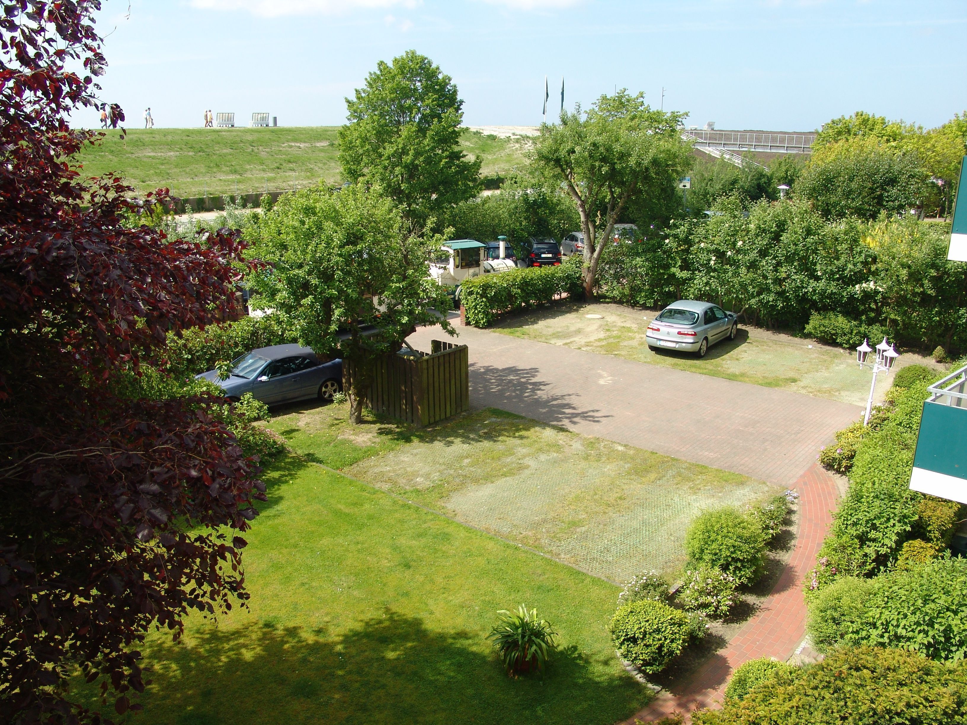 A parking area with cars, a wooden fence, and a grassy field.
