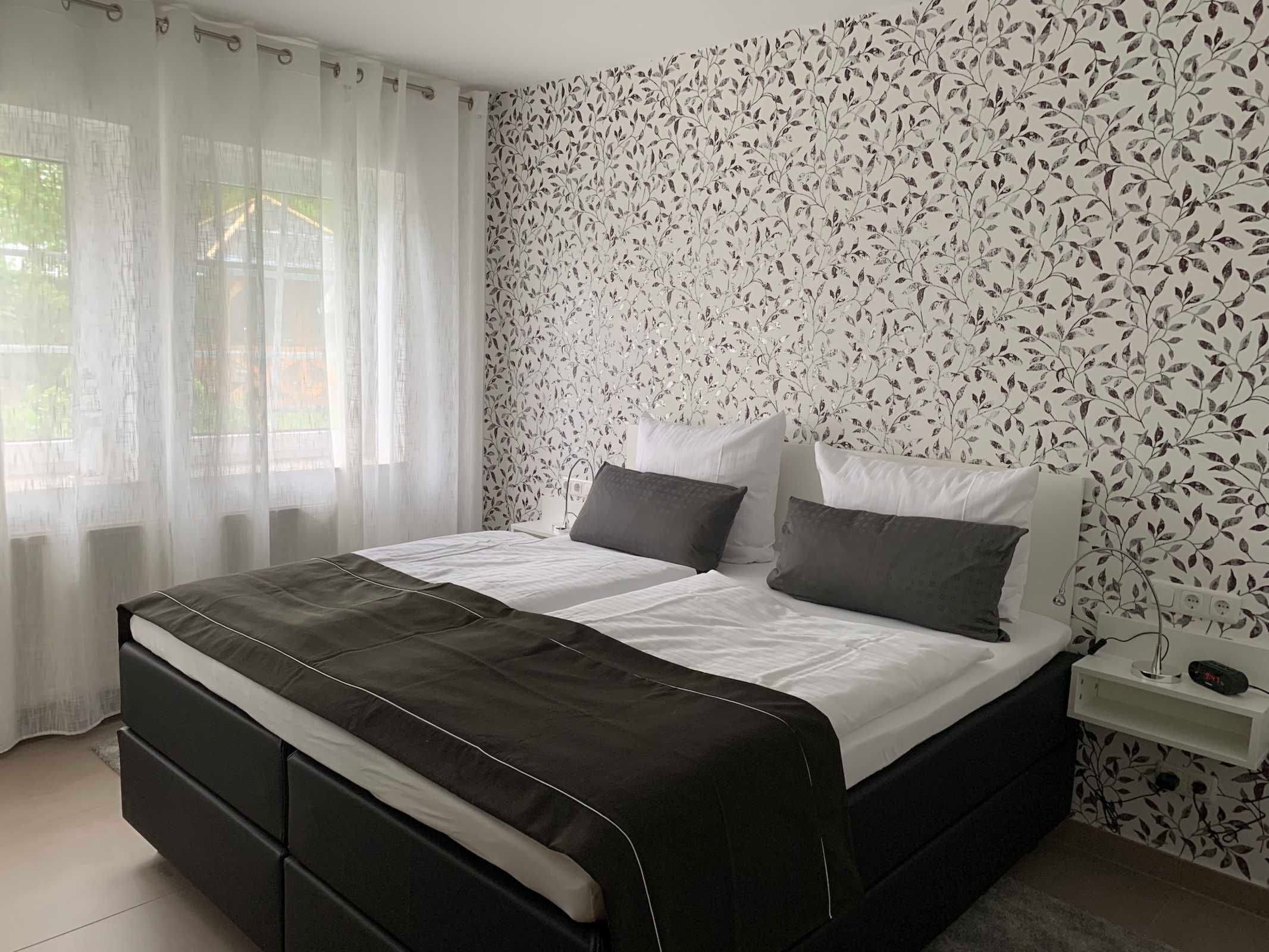 Una camera da letto moderna con un letto nero, biancheria da letto bianca e un motivo floreale alle pareti.