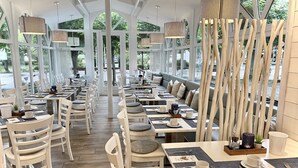 A restaurant with white chairs and tables, a wooden floor, and hanging lights. - 15 Ferienappartement Mönchgut (A) - Apartment house Haus Arkona (Sellin)