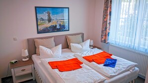 En dubbelsäng med vita sängkläder, randiga kuddar och orangea och blå handdukar. En tavla med ett landskapsmotiv hänger ovanför sängen.