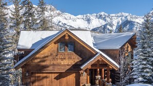 A wooden cabin with a snow-covered roof, set against a backdrop of snow-capped mountains. - MOUNTAIN MELODY- A Luxury Music Paradise, On Elks Pond, Hot Tub, Oxygen Bar (Telluride)