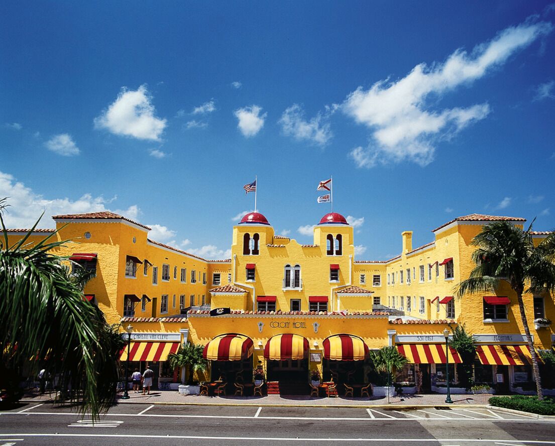 A yellow building with red and white striped awnings, a prominent entrance, and flags on top.