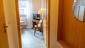 A hallway leading to a room with a wooden door, a round mirror, and a bed with a white headboard. - Single Room (21) - Pension Zur Curve (Prohn)