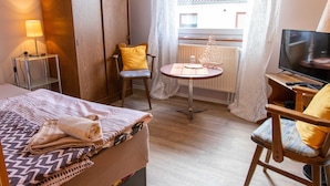 A hotel room with a bed, a chair, a small table, a TV, and a window with curtains. - Single Room (21) - Pension Zur Curve (Prohn)