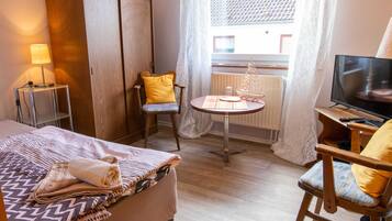 Ein Hotelzimmer mit Bett, Sessel, kleinem Tisch, Fernseher und einem Fenster mit Vorhängen.