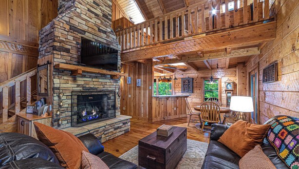 A cozy log cabin interior with a stone fireplace, leather sofas, and a dining area. - Luxury cabin in the woods, 2 bedrooms plus loft (Fairfield)