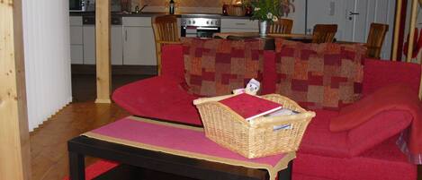 A cozy living room with a red sofa, a coffee table, and a kitchen in the background.
