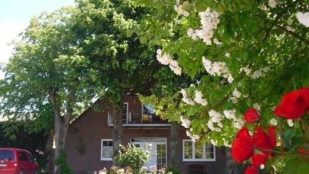 Une maison à deux étages, construite en briques, avec un jardin devant et une voiture rouge garée devant.