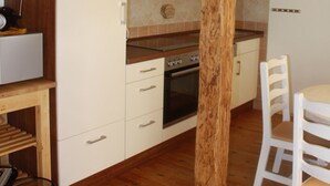 Une cuisine avec des meubles blancs, un plafond avec une poutre en bois et un coin repas avec des chaises blanches.