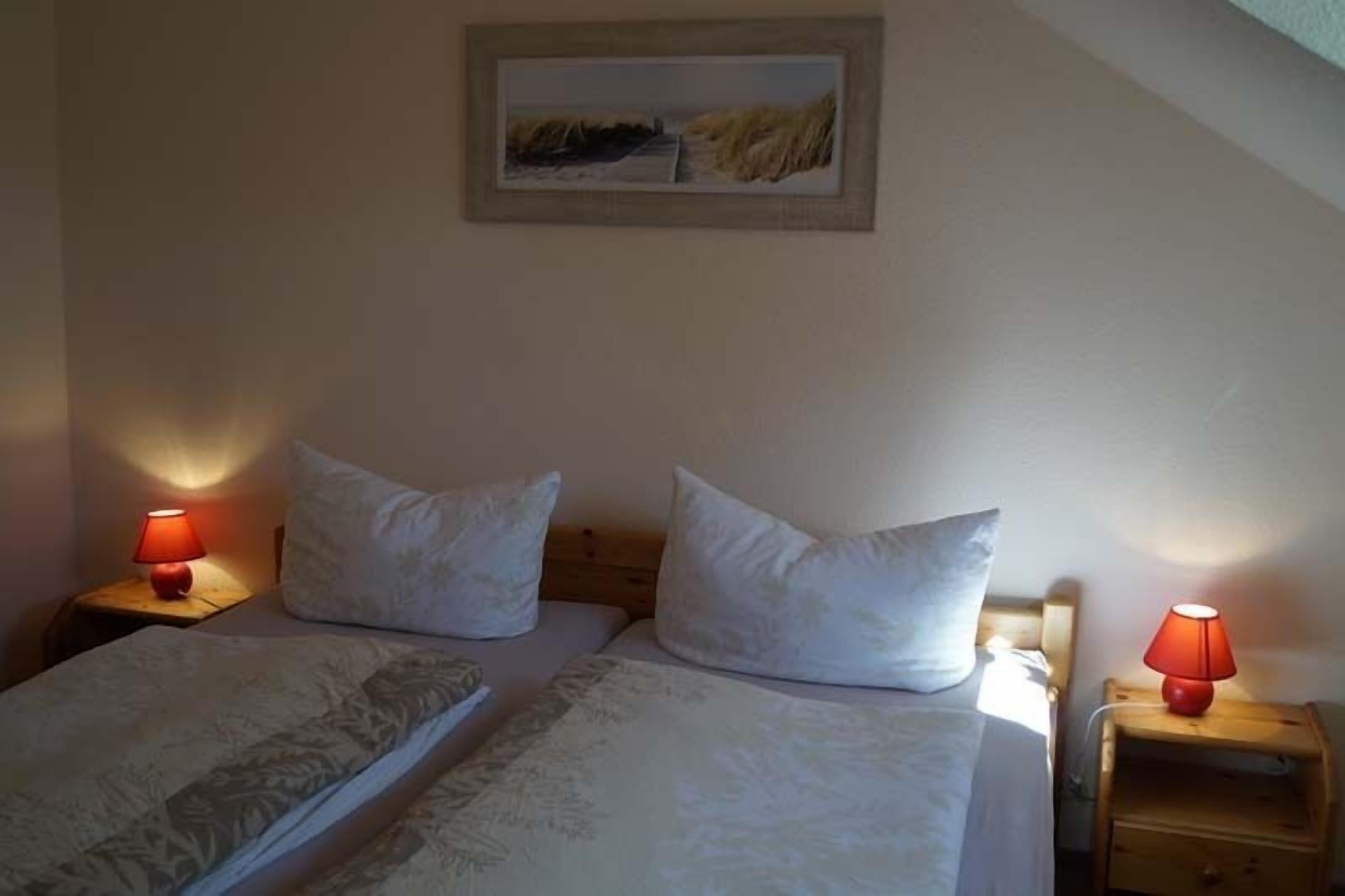 A bedroom with two beds, each with a pillow and a red lamp on a wooden nightstand.