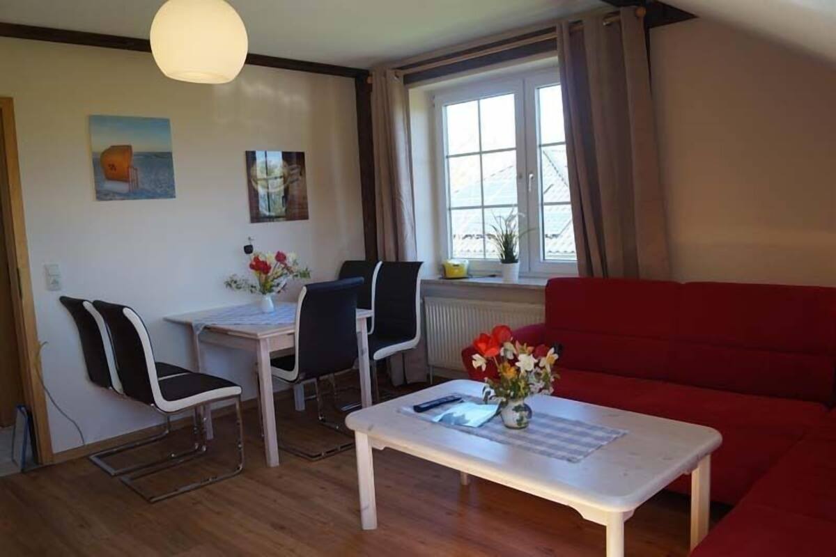 A living room with a red sofa, a white coffee table, and a dining area with a table and chairs.