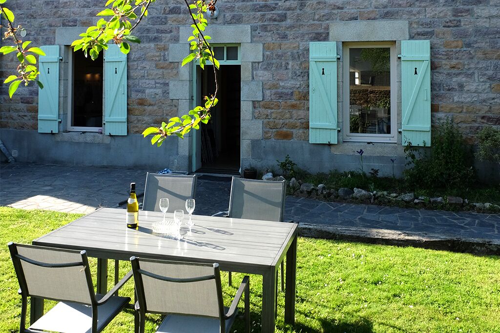 Ein Essbereich im Freien mit Tisch und Stühlen, einer Weinflasche und zwei offenen Fenstern mit Fensterläden.