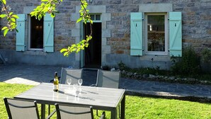 An outdoor dining area with a table and chairs, a bottle of wine, and two open windows with shutters. - The Hauts de Kerity, 1920's house by the sea (Paimpol)