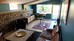 A cozy living room with a stone wall, a wooden table, a leather sofa, and a dining area with a table and chairs. - The Hauts de Kerity, 1920's house by the sea (Paimpol)
